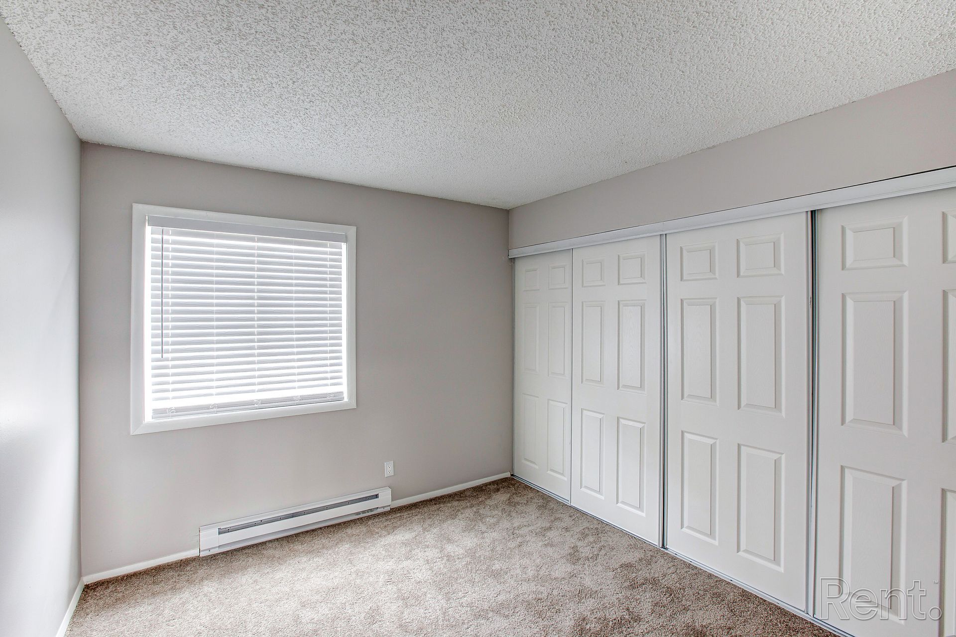Empty bedroom with a window, white closet doors, and beige carpet.