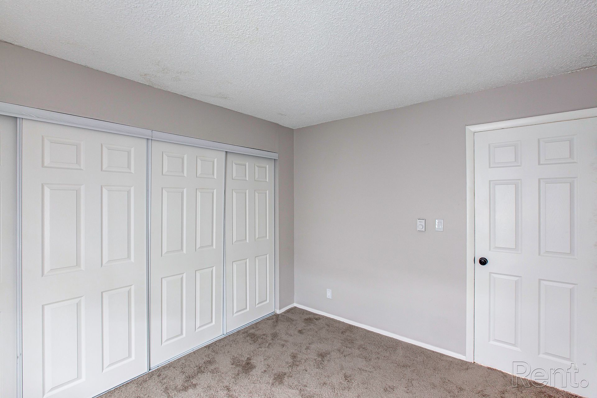 Empty bedroom with sliding closet doors, a door, grey walls, and carpet.