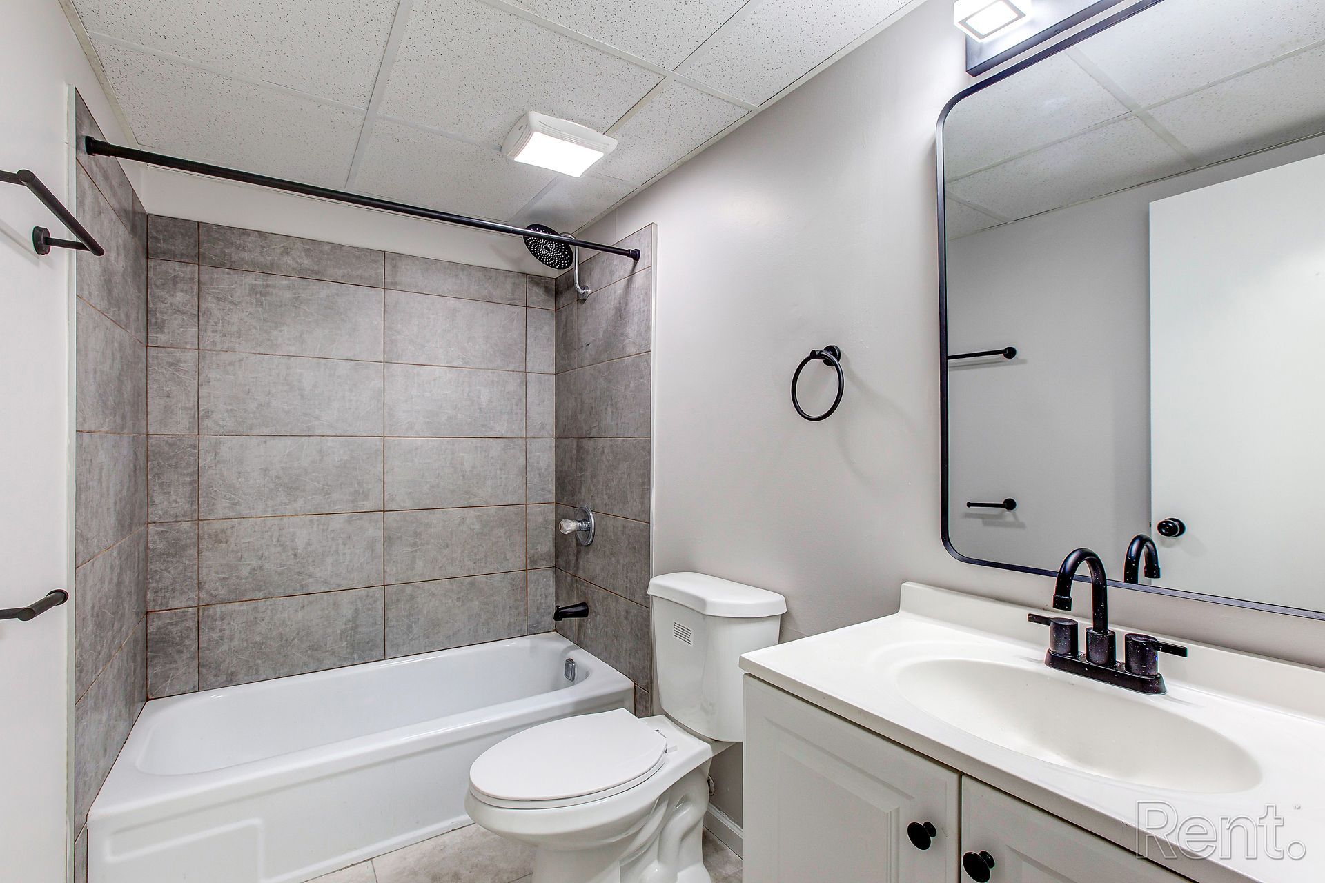 Modern bathroom with gray tiled shower, white vanity, toilet, and black fixtures.