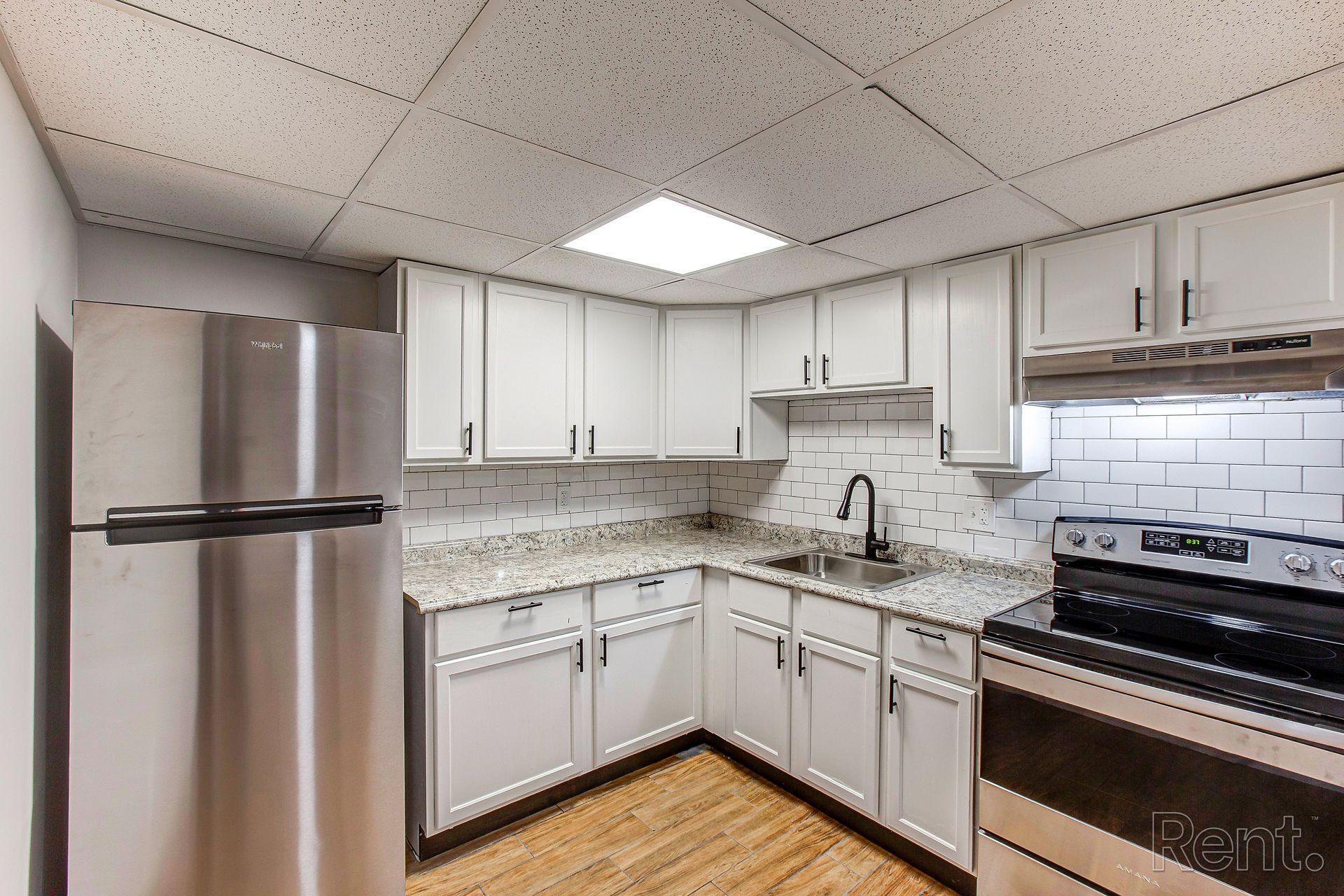 White kitchen with stainless steel appliances, countertops, white cabinets, and a black faucet.
