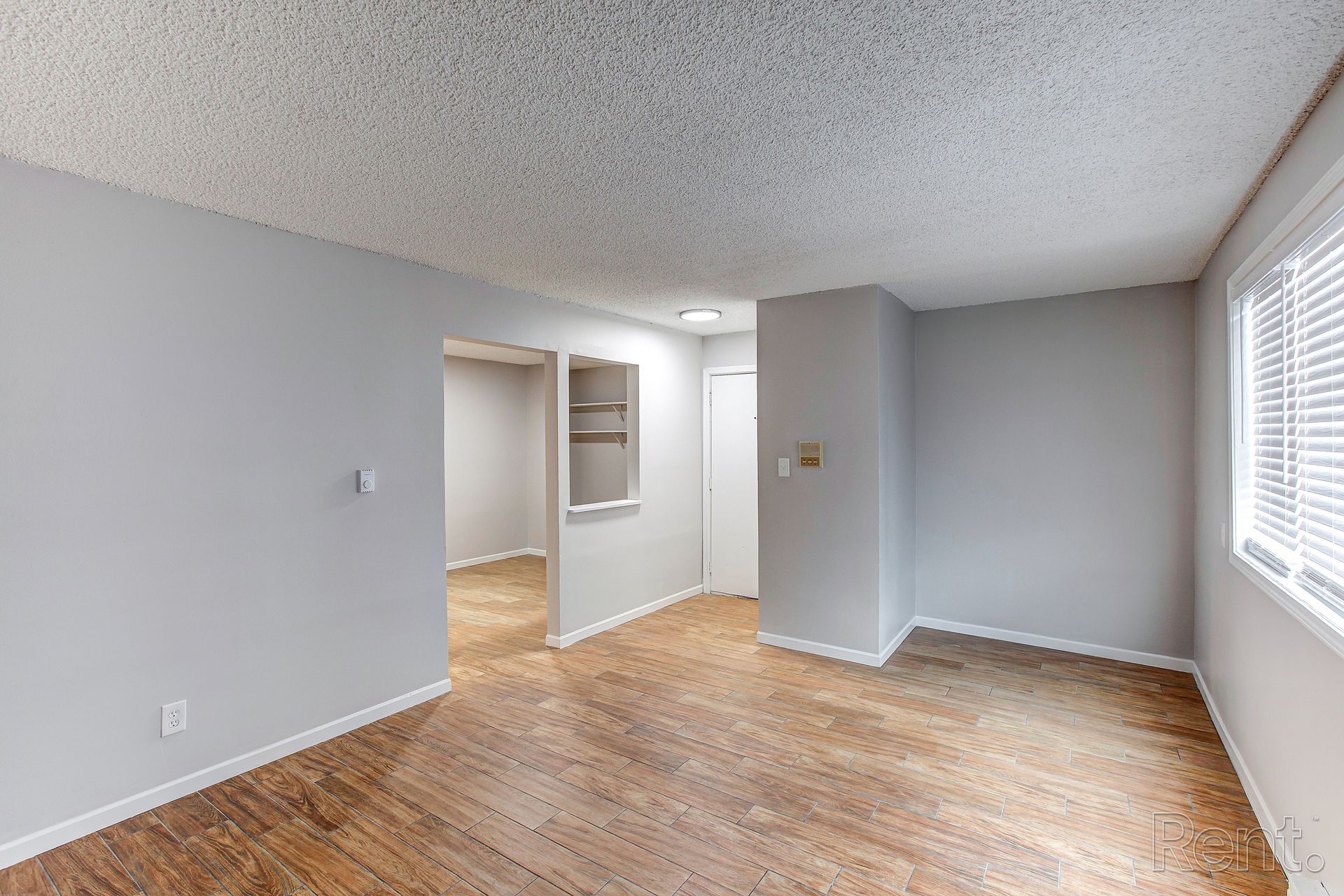Empty apartment interior with light gray walls, wood flooring, and a window.