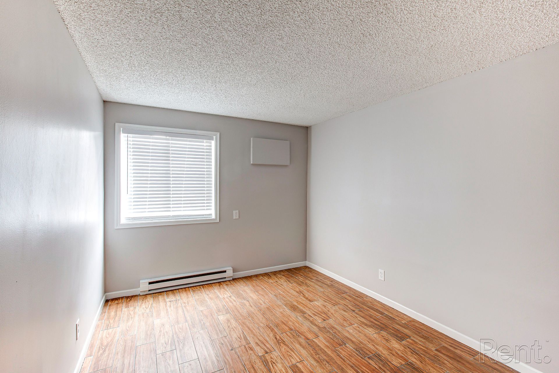 Empty room with wood-look flooring, white walls, window with blinds, and textured ceiling.