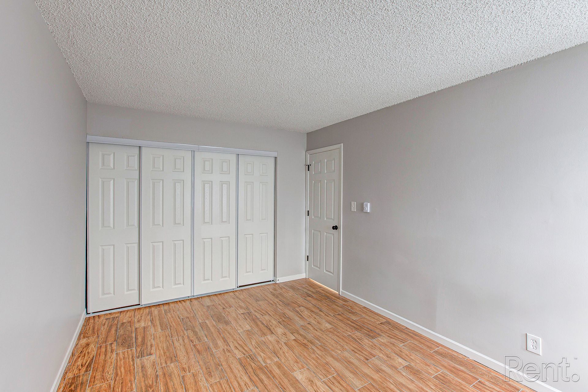 Empty room with white bi-fold closet doors, wood floor, light gray walls, and white ceiling.