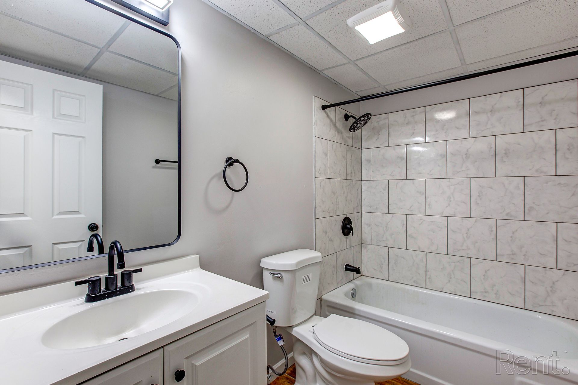 Bathroom with white vanity, toilet, and bathtub, gray walls, and black fixtures.
