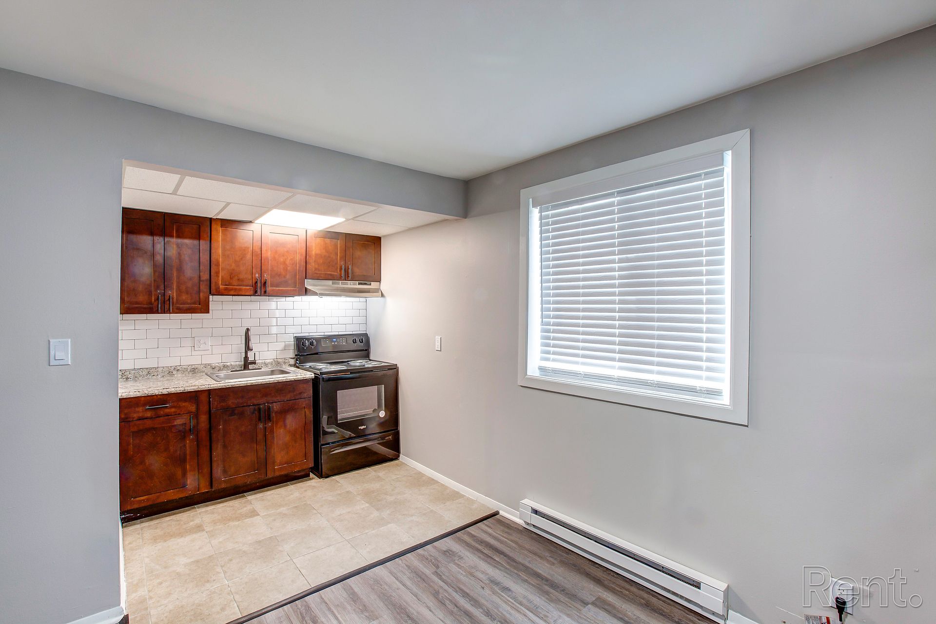 Small kitchen with brown cabinets, gray walls, window with blinds, and a stove.