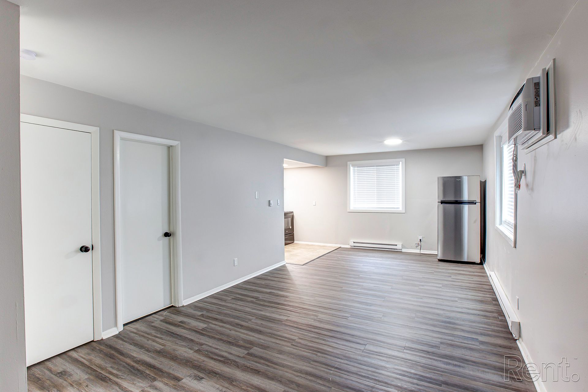 A renovated room with grey flooring and walls, two white doors, a refrigerator, and a window.