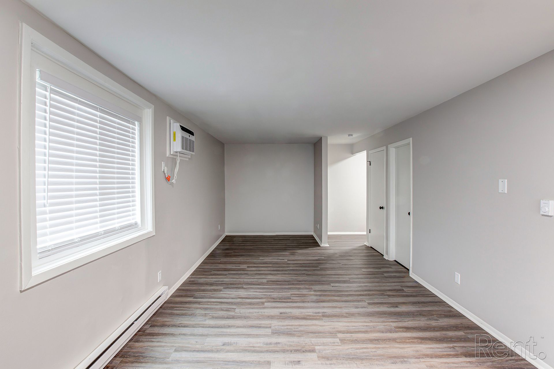 Empty room with gray walls, wood-look floor, window with blinds, and doorway.