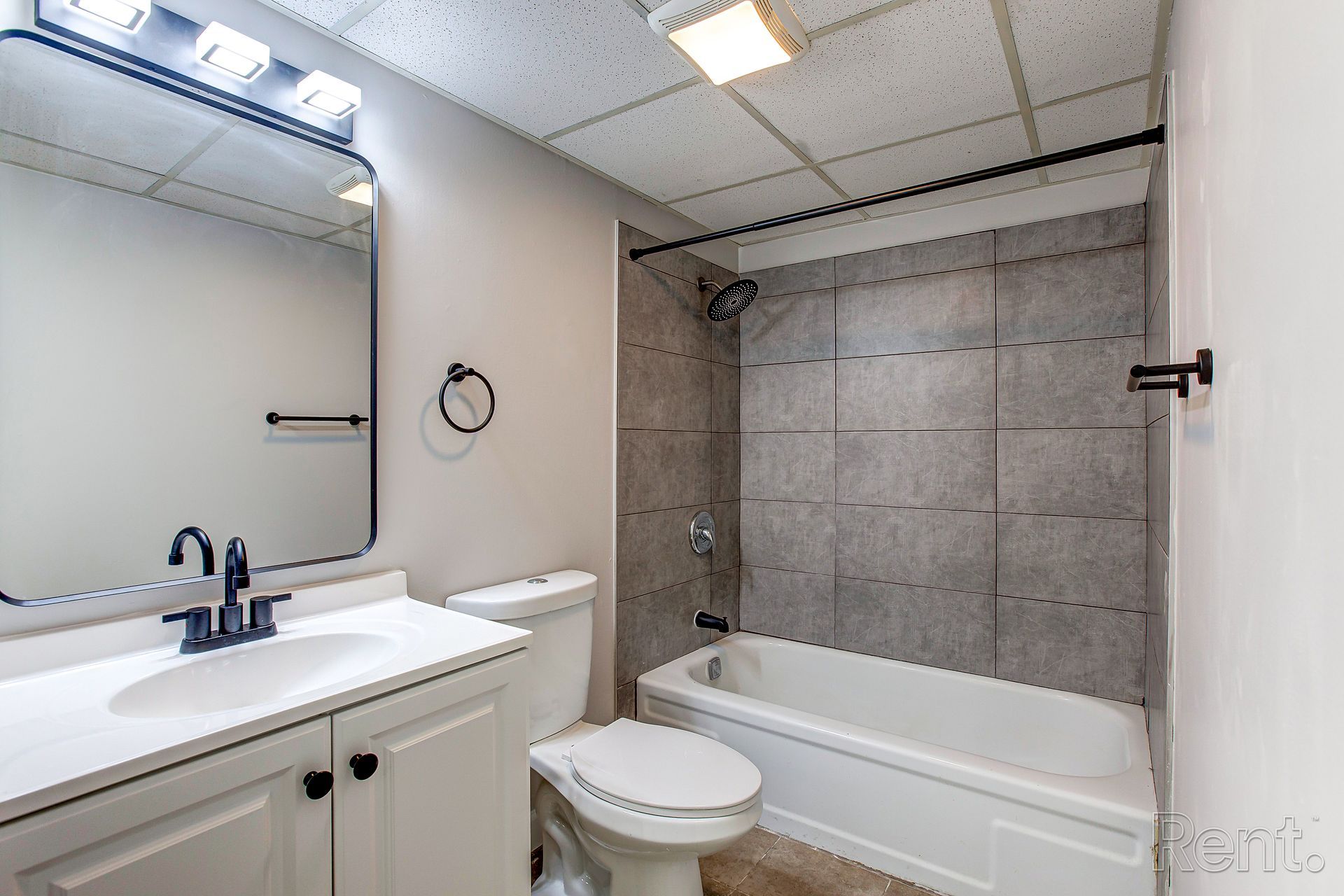 Bathroom with a white vanity, toilet, bathtub, and gray tiled shower walls.