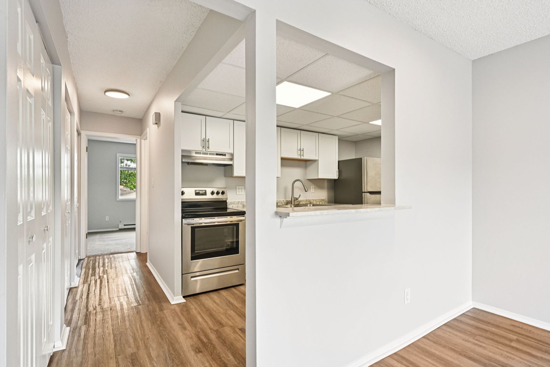 Hallway view into a kitchen with stainless steel appliances and white cabinets.