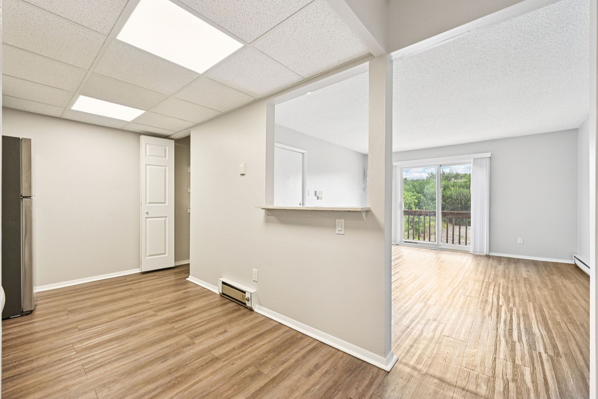 Interior view of an apartment with hardwood floors, a doorway, and a sliding glass door to a balcony.