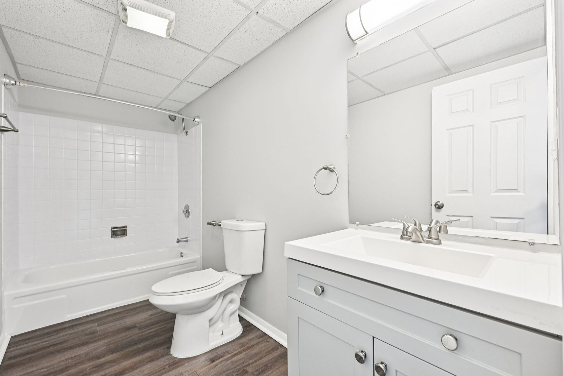 Bathroom with a white tub, toilet, sink, and gray vanity, featuring wood-look flooring.