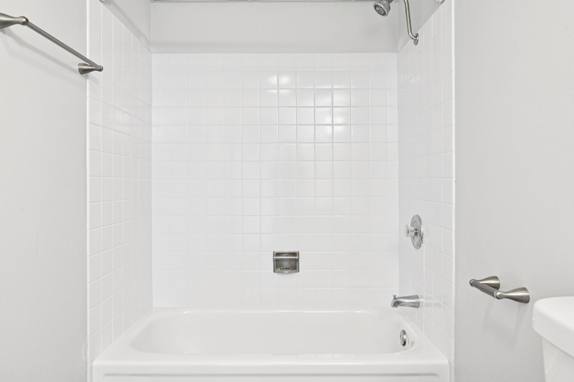 White bathroom with a tub, shower, and tiled walls. A towel rack and toilet are visible.