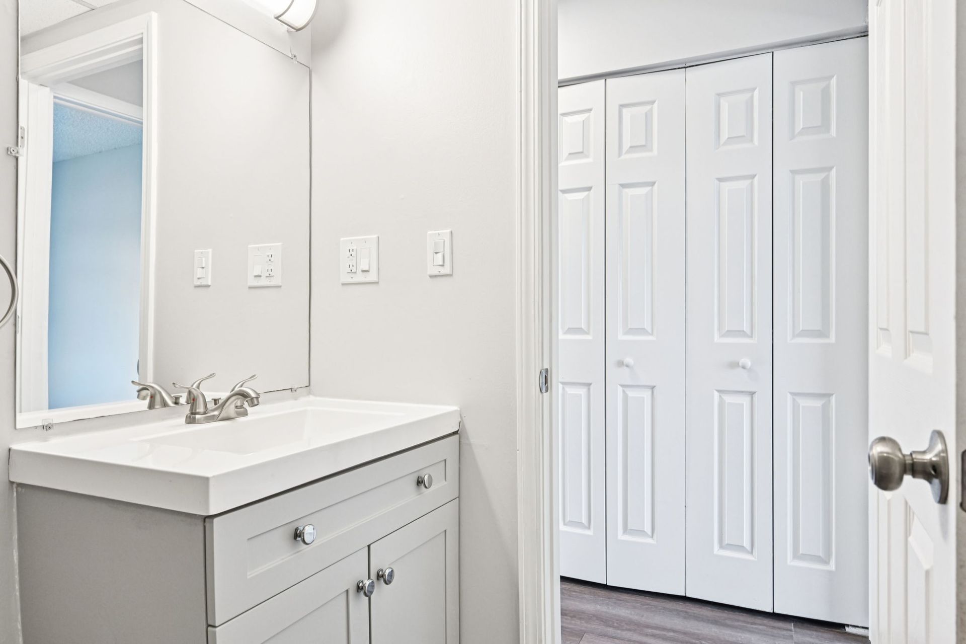 Bathroom with light gray vanity and white bi-fold closet doors.