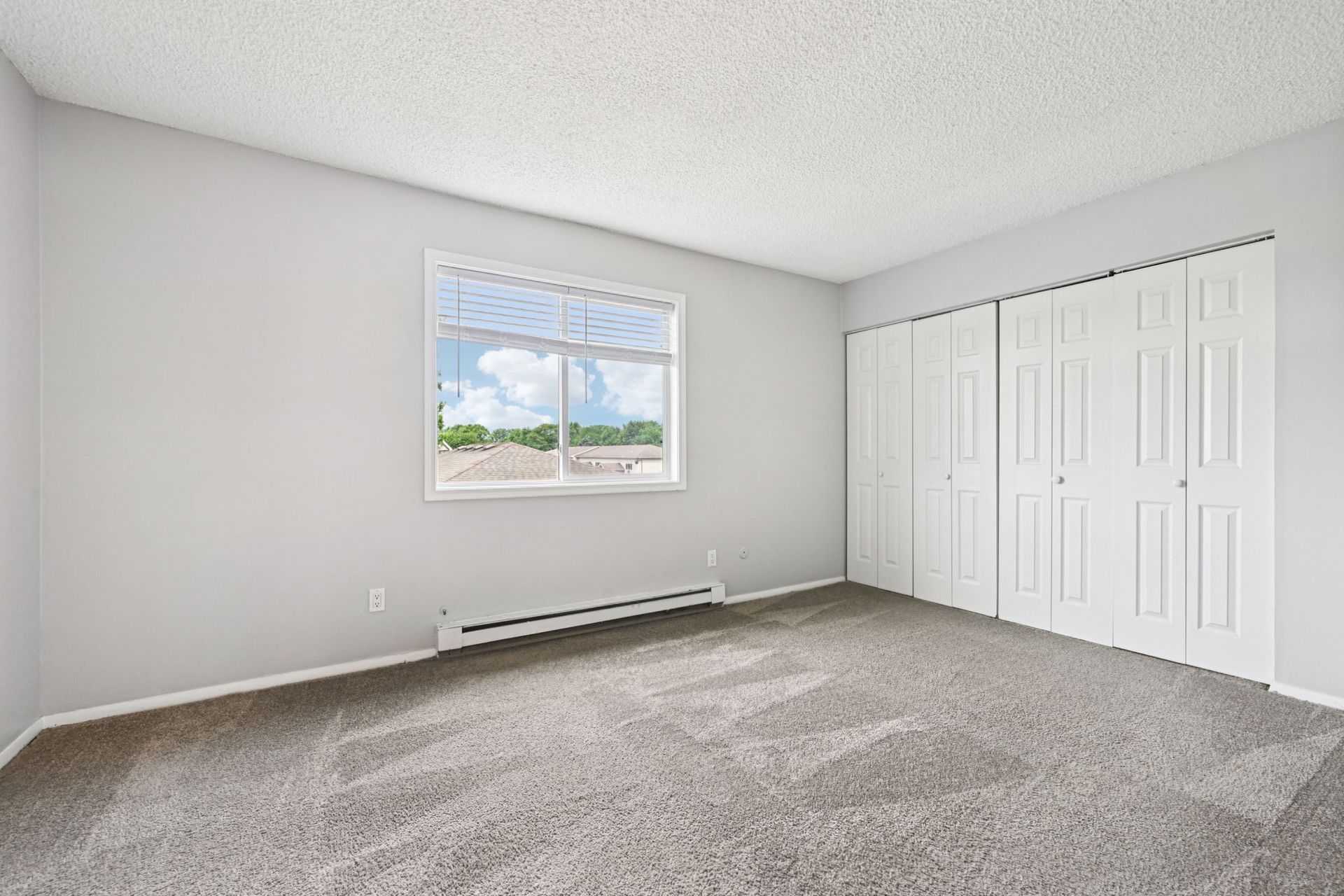 Empty bedroom with gray walls, carpet, white closet doors, and a window with a view.
