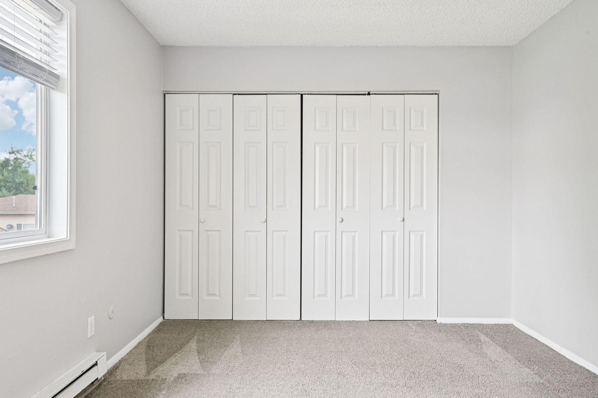Empty bedroom with gray walls, white closet doors, carpet, and a window.