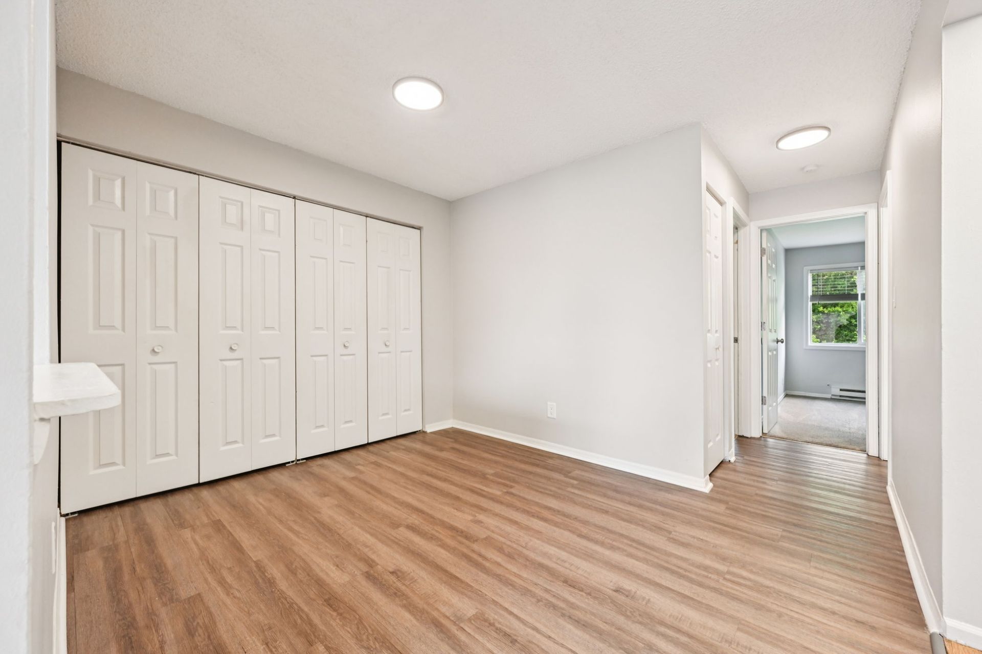 Empty room with white closet, light wood floor, gray walls, and an open doorway to another room.