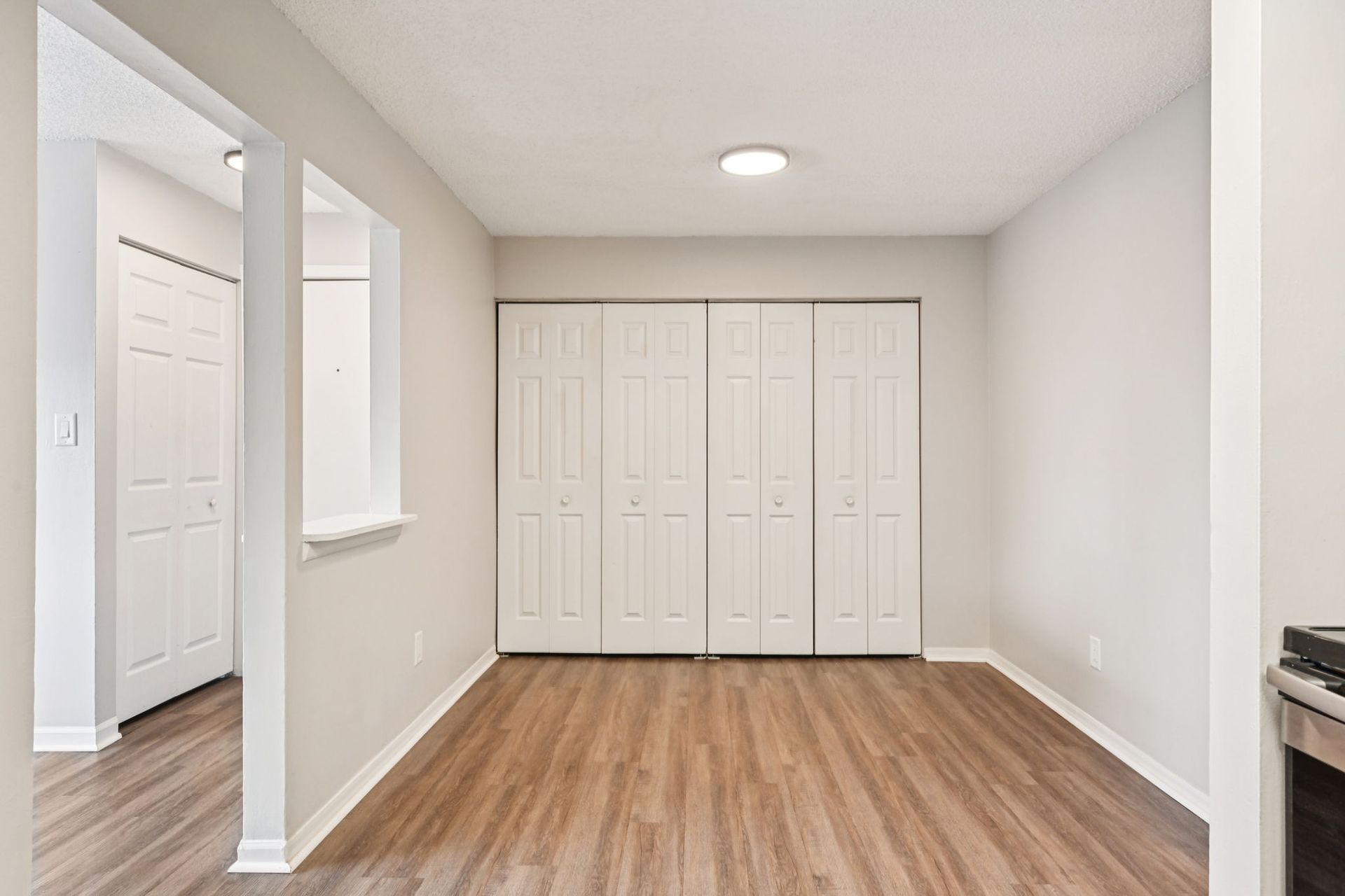 Empty room with wood-look flooring, white closet doors, and doorway to another room.