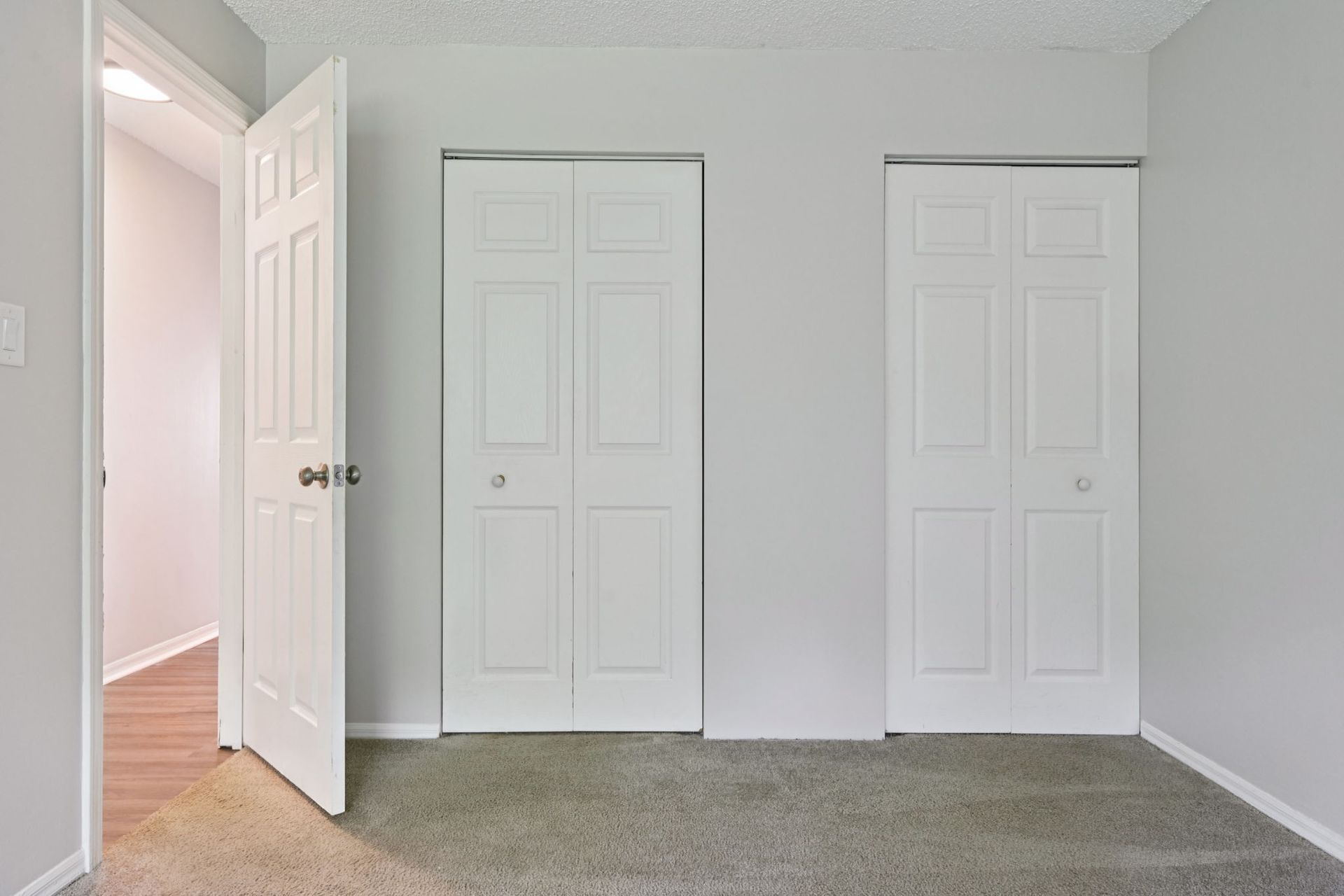 A room with light gray walls, two white closet doors, and an open white door on the left.