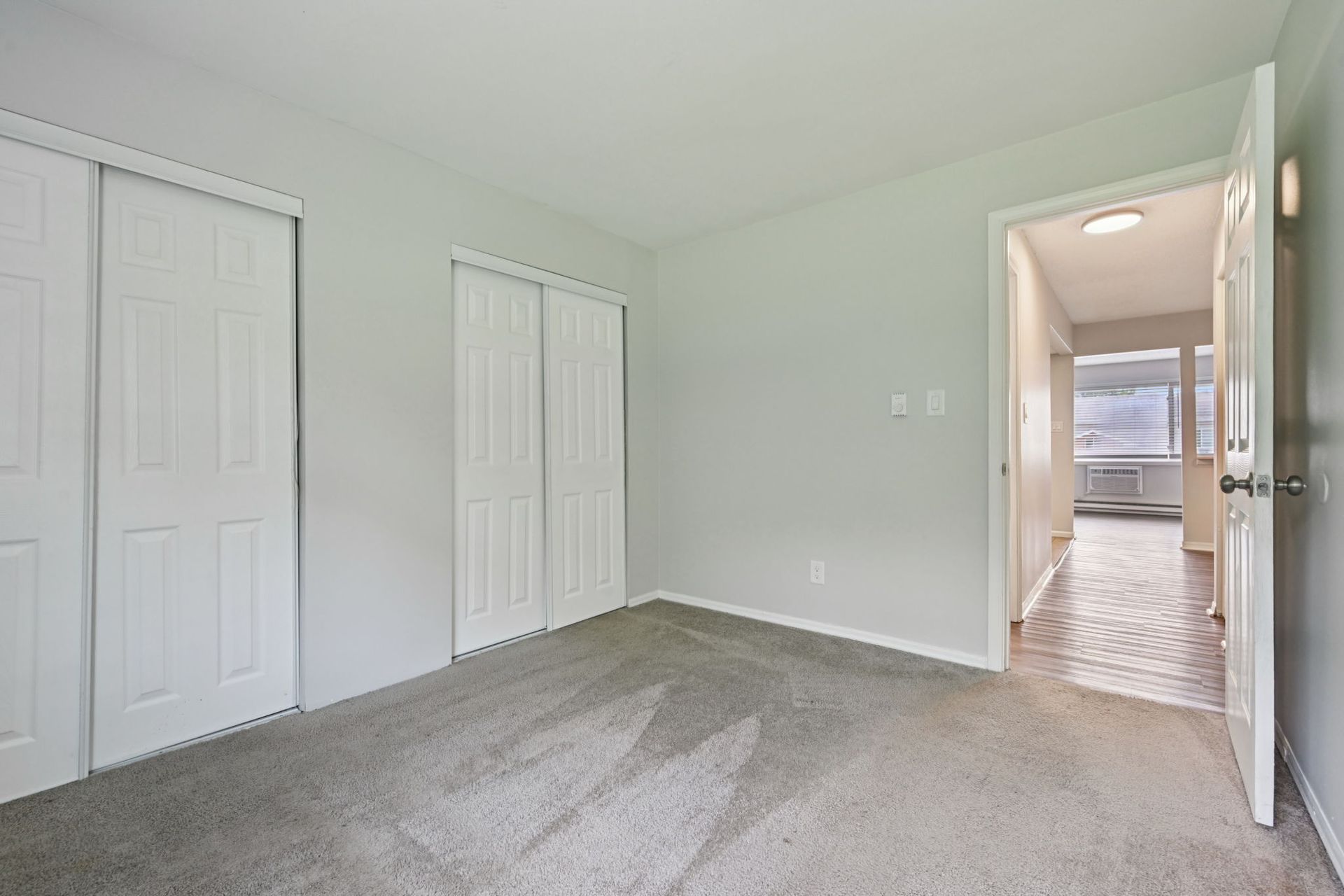Empty bedroom with gray walls, carpet, white closet doors, and an open doorway to a hallway.
