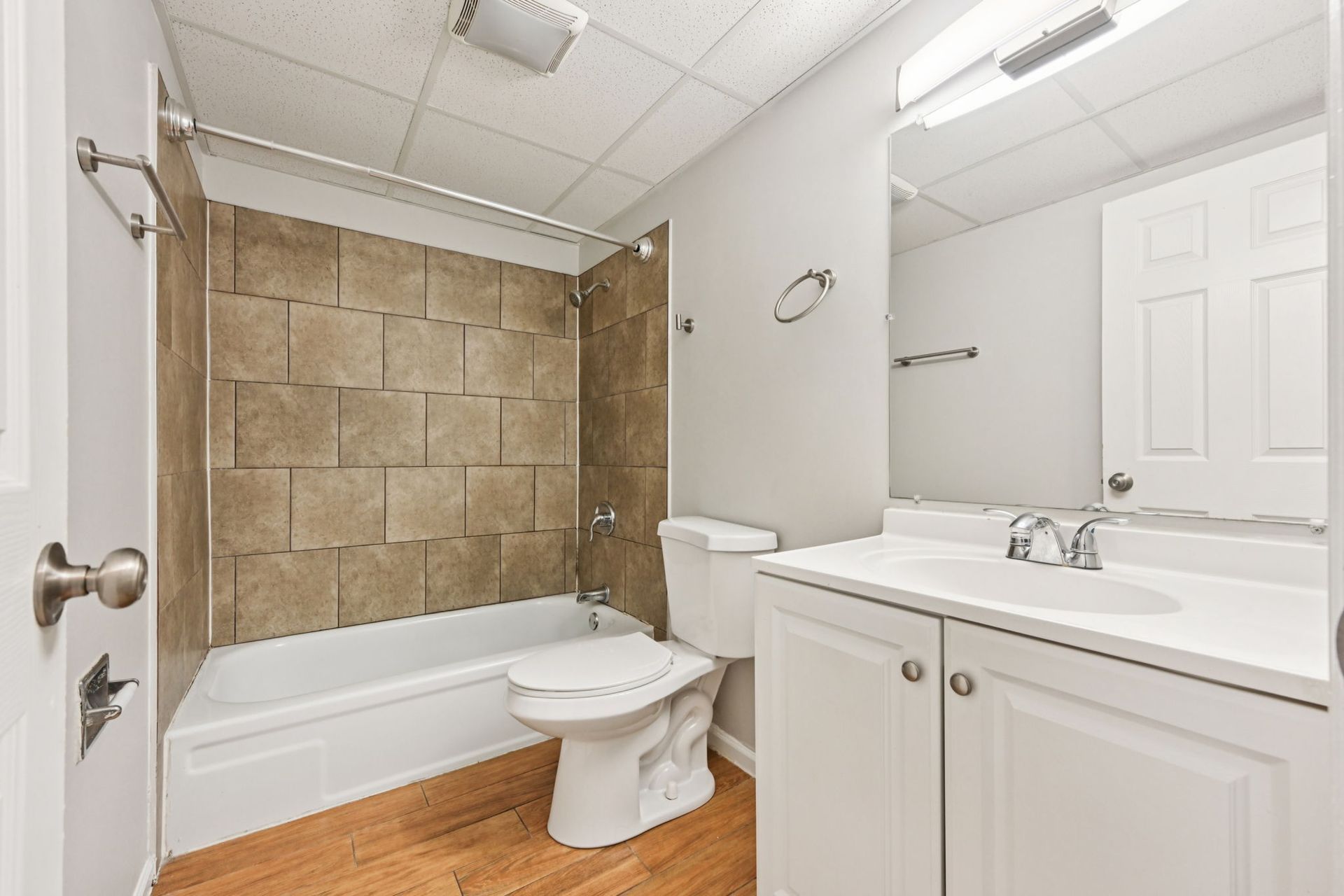 Bathroom with white vanity, toilet, and bathtub with tan tile surround; light wood flooring.
