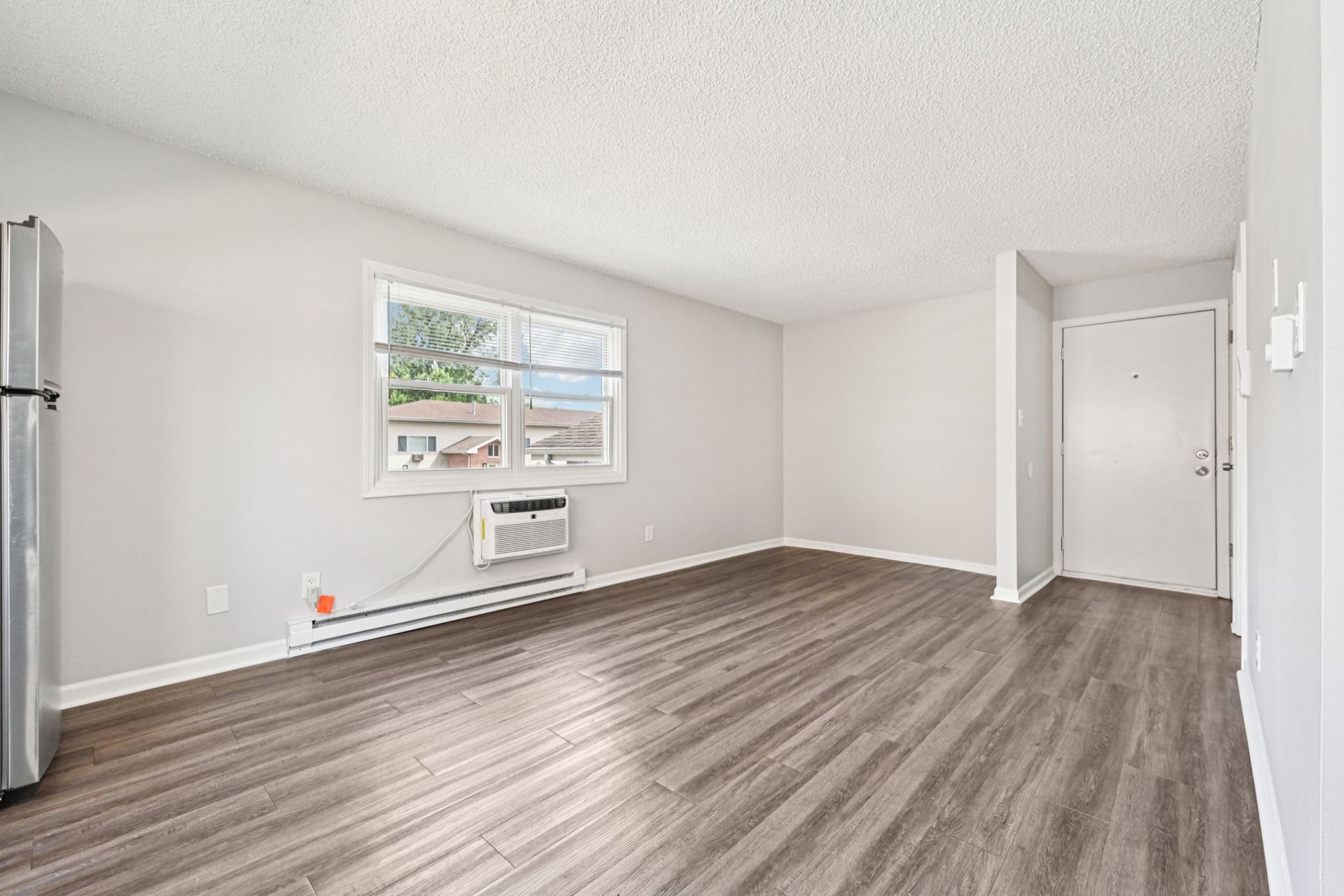 Empty apartment living room with window, air conditioner, and wood-look flooring.