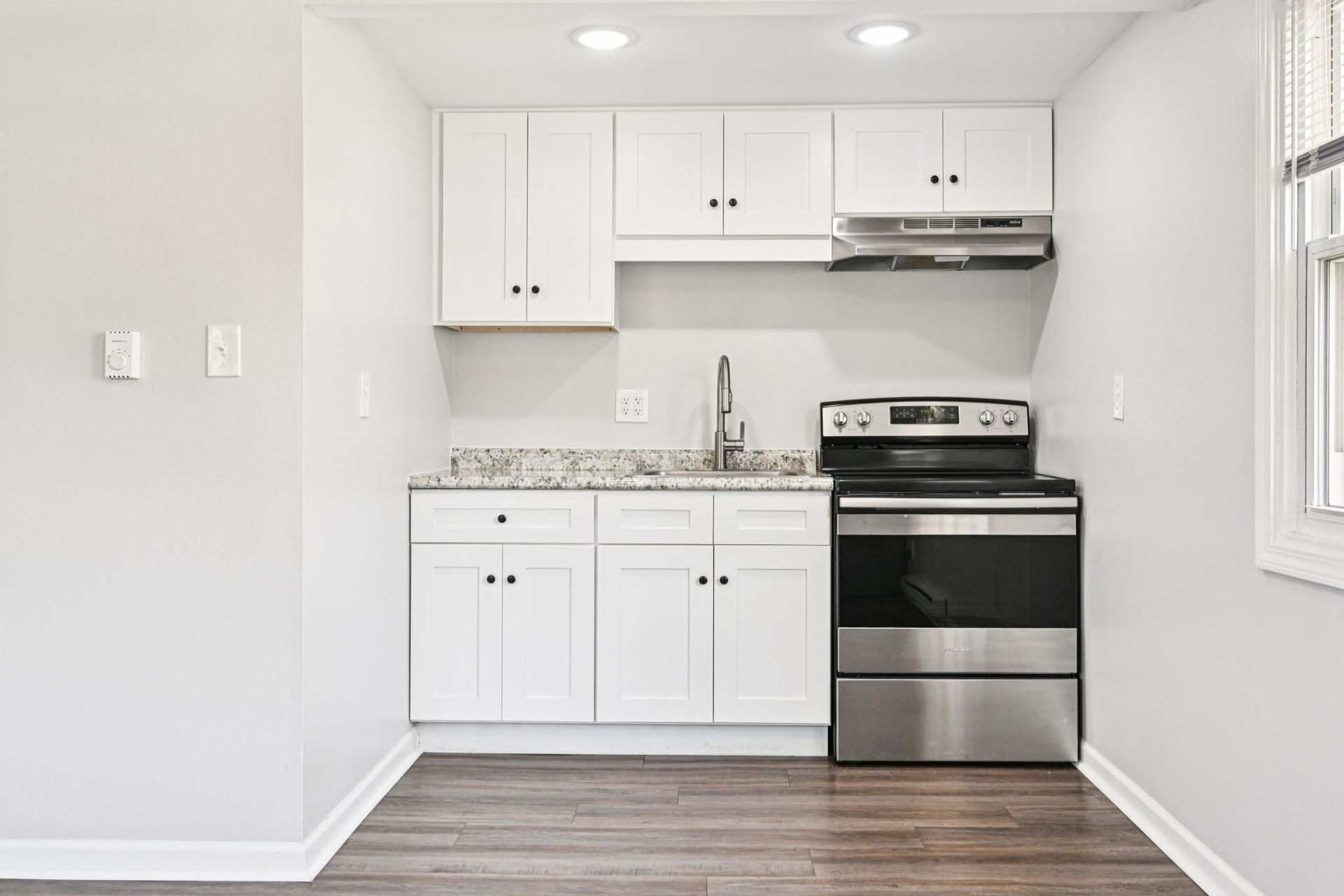 Small, white kitchen with stainless steel appliances and speckled countertops.