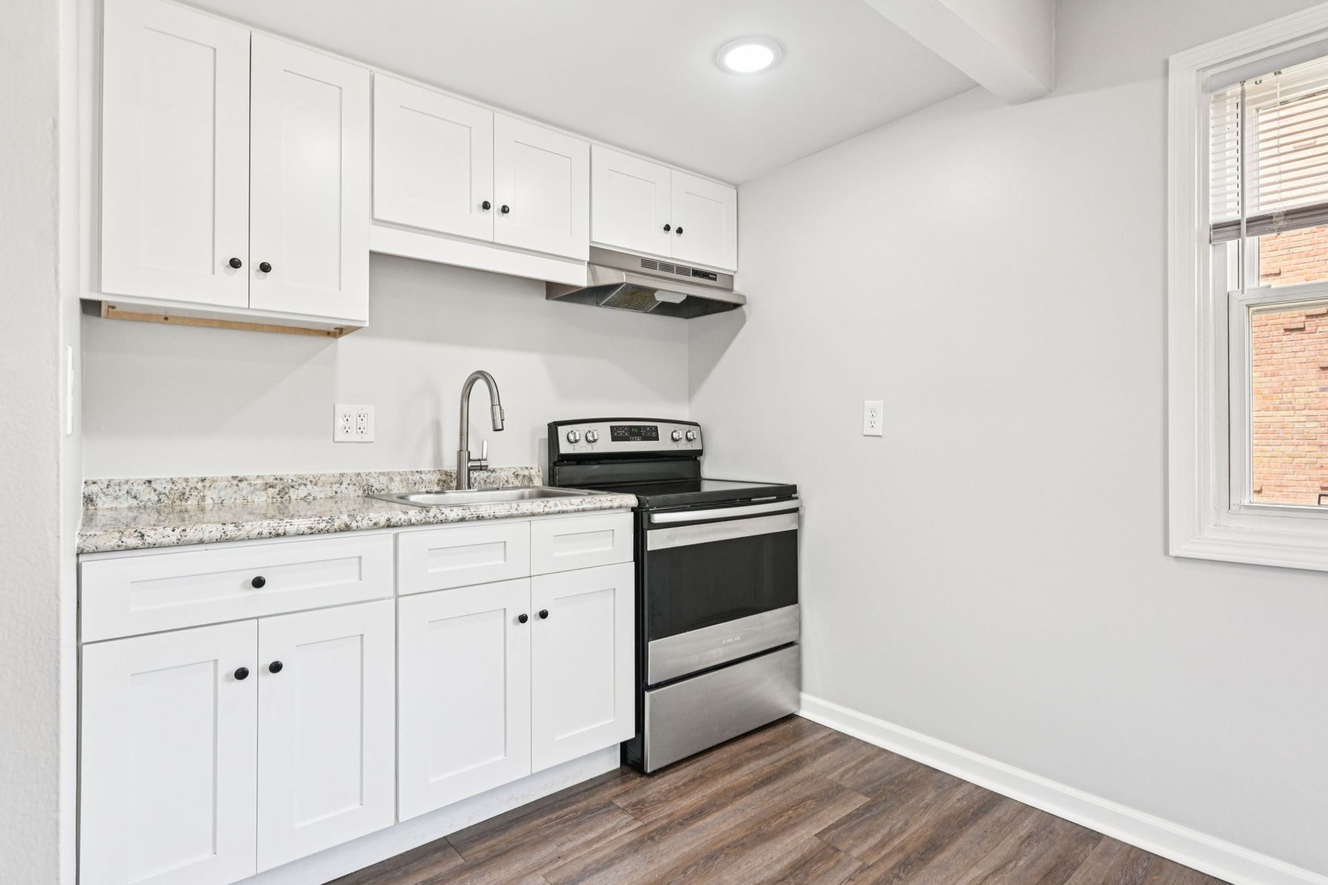 Small, white kitchen with stainless steel appliances and granite countertops.