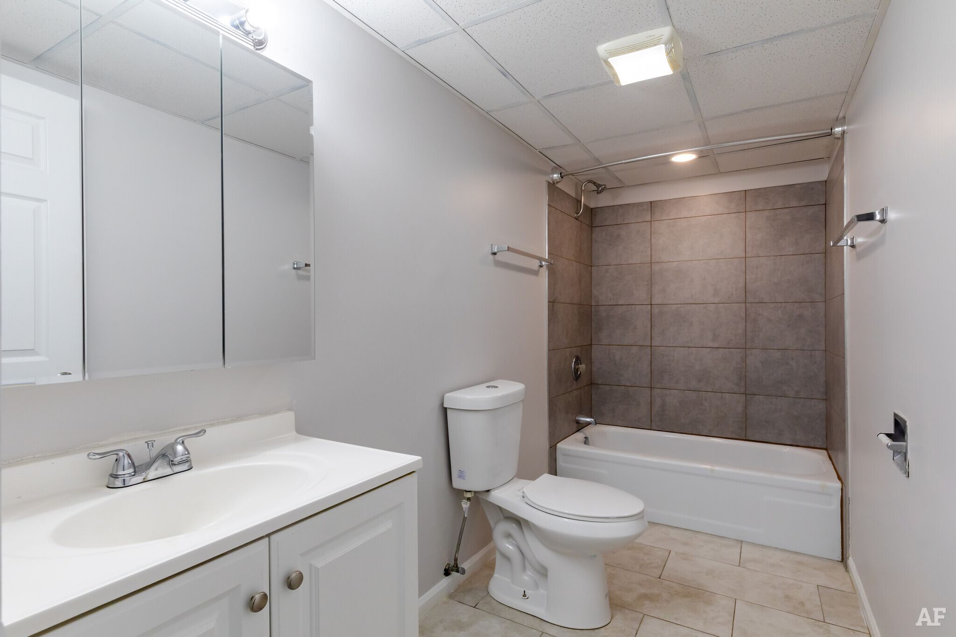 Bathroom with a white vanity, toilet, and bathtub. Gray walls, tiled shower surround, and a mirrored cabinet.