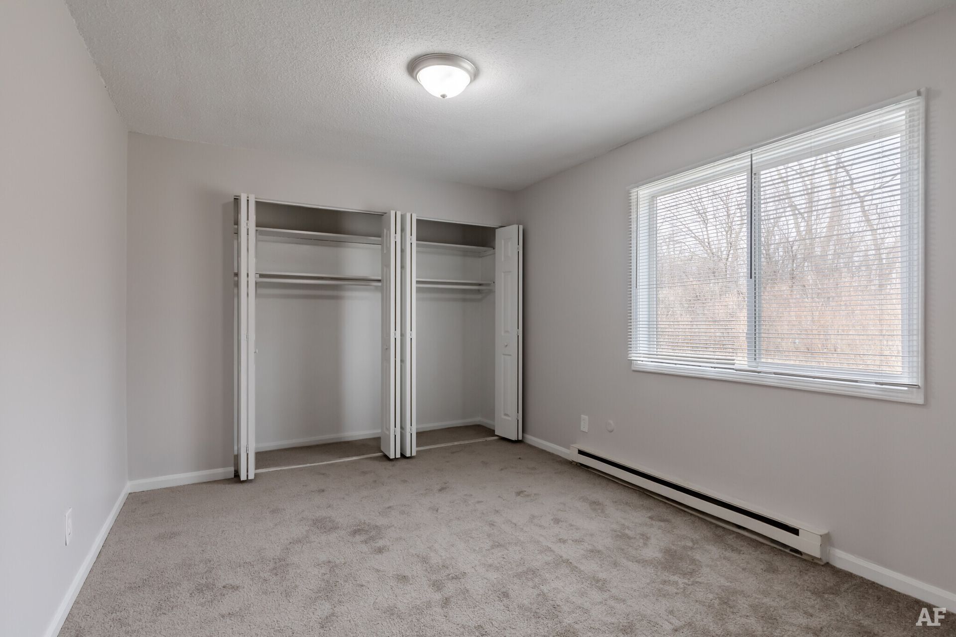 Empty bedroom with two closets, a window, and gray carpet.