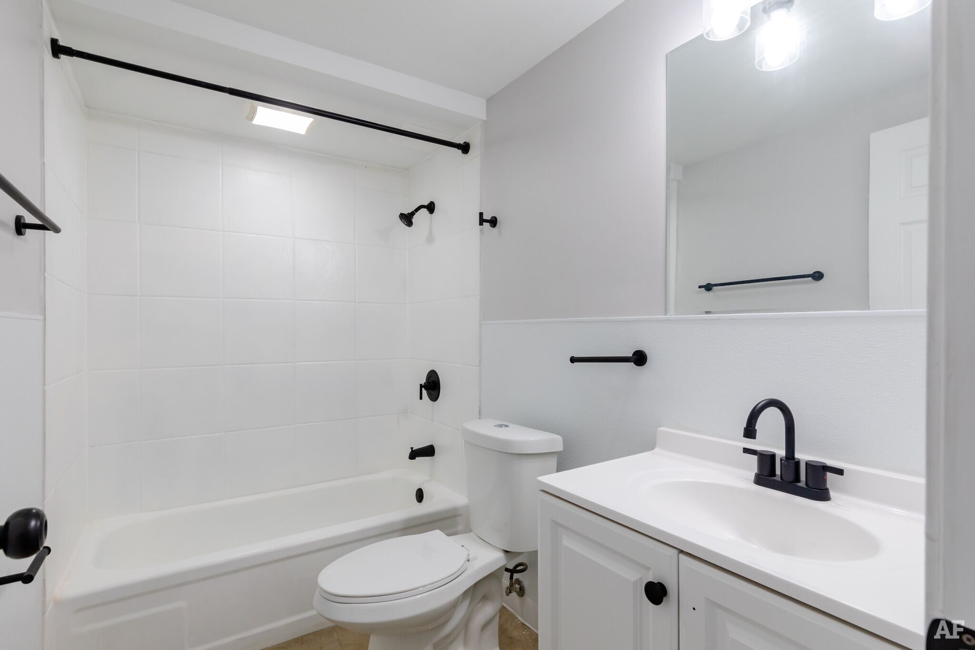 White bathroom with black fixtures, tub, sink, and toilet.