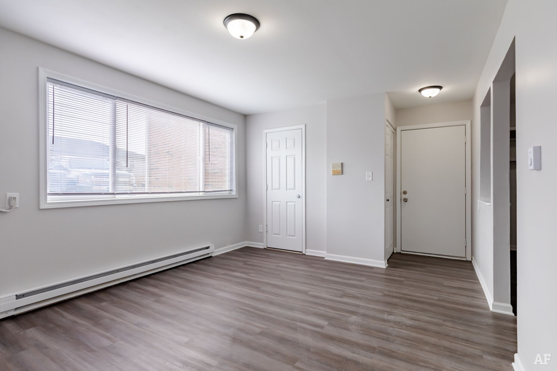 Empty living room with gray walls, wood floors, and a window with blinds.