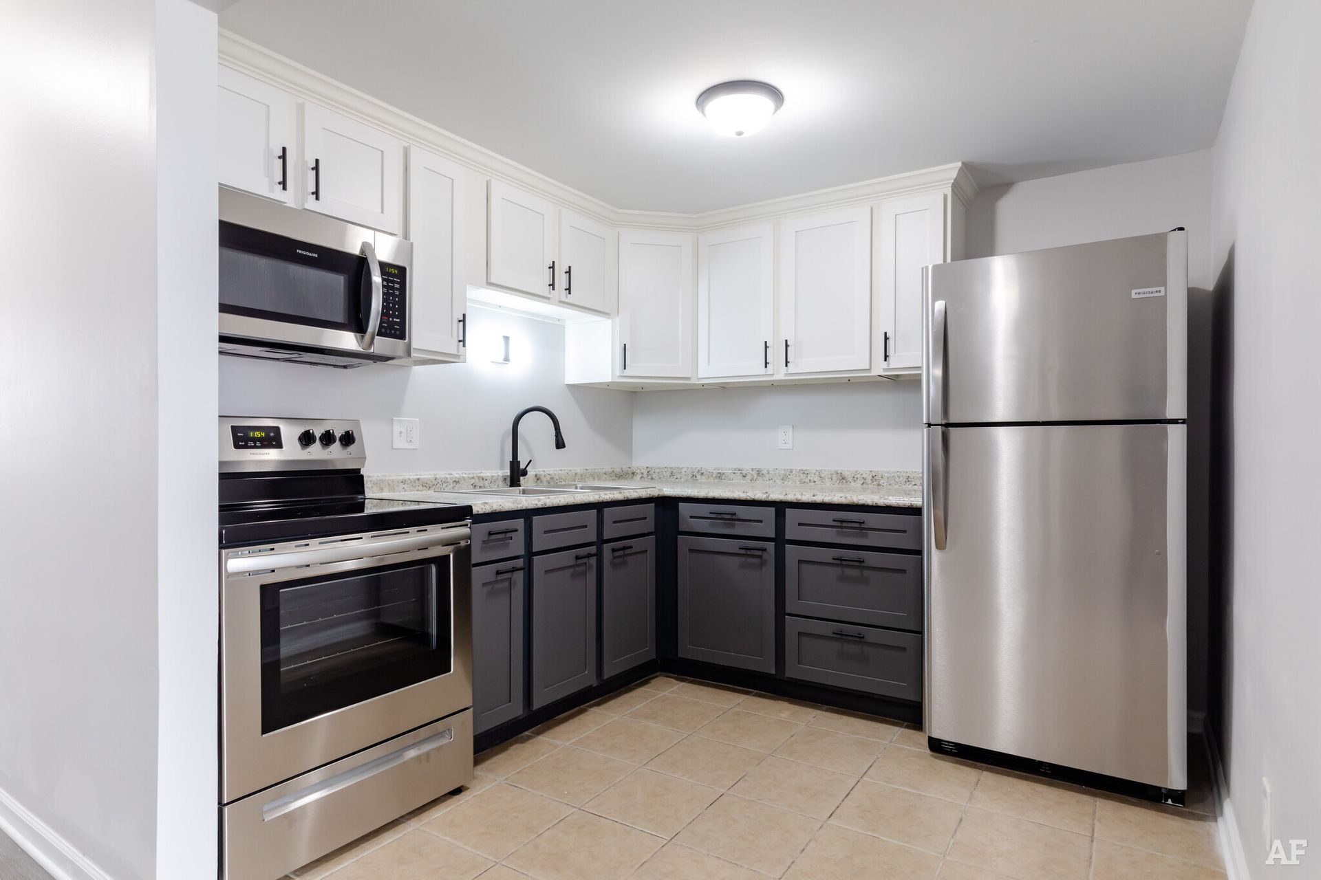 A modern kitchen with stainless steel appliances, white upper cabinets, gray lower cabinets, and a light countertop.