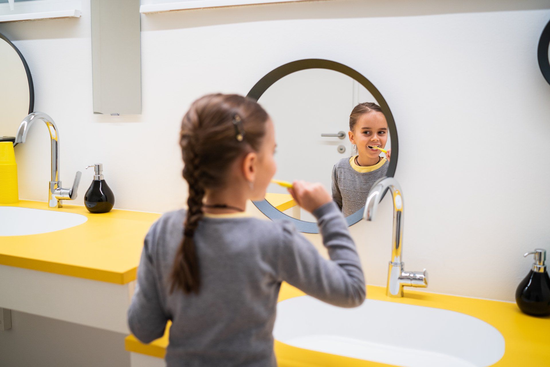 Ein kleines Mädchen putzt sich vor einem Spiegel die Zähne.