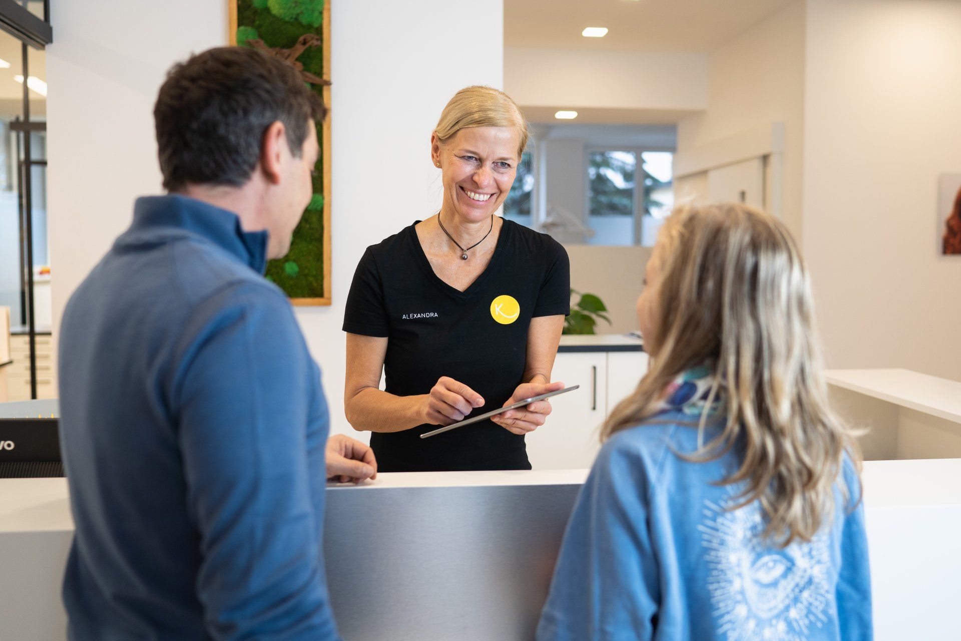 Eine Mitarbeiterin lächelt, während sie mit einem Mann und einem Mädchen spricht