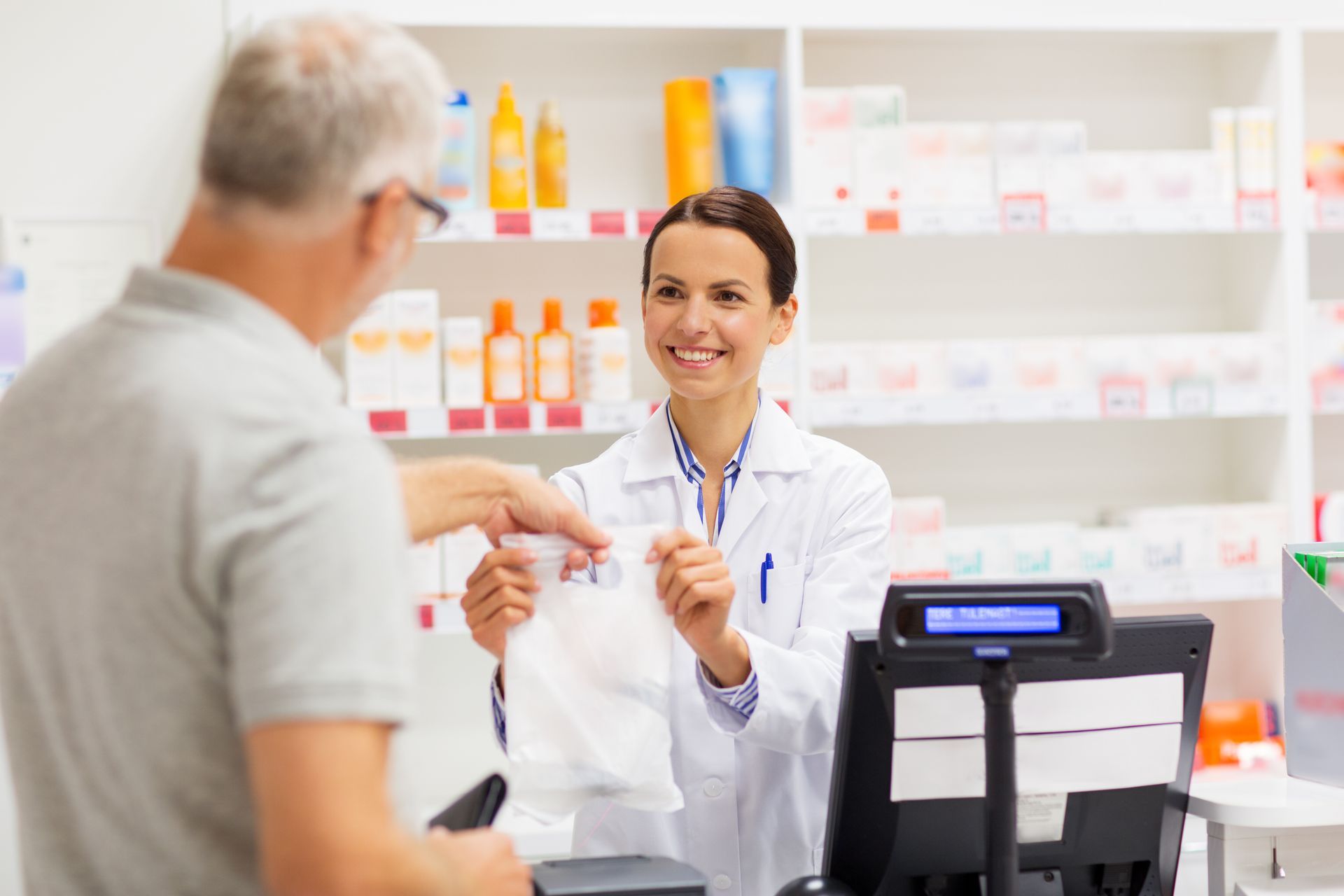 Pharmacy staff handing a packaged item to a customer at the counter. Pharmacy staff handing a packaged item to a customer at the counter.