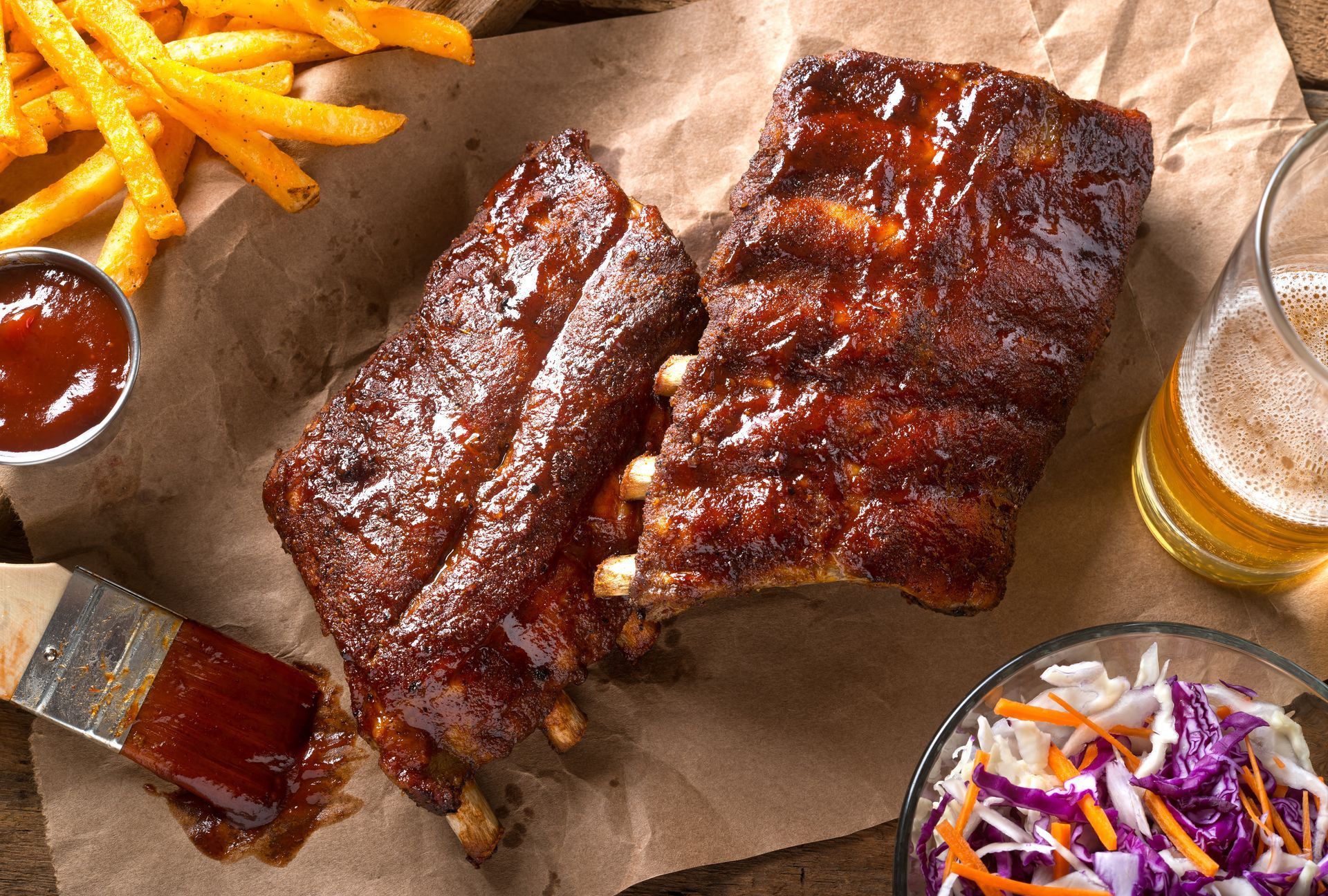 ribs , french fries , coleslaw and a glass of beer on a table .