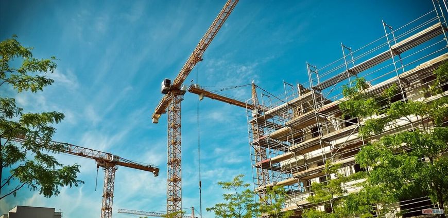 Construction site with cranes and building under blue sky.