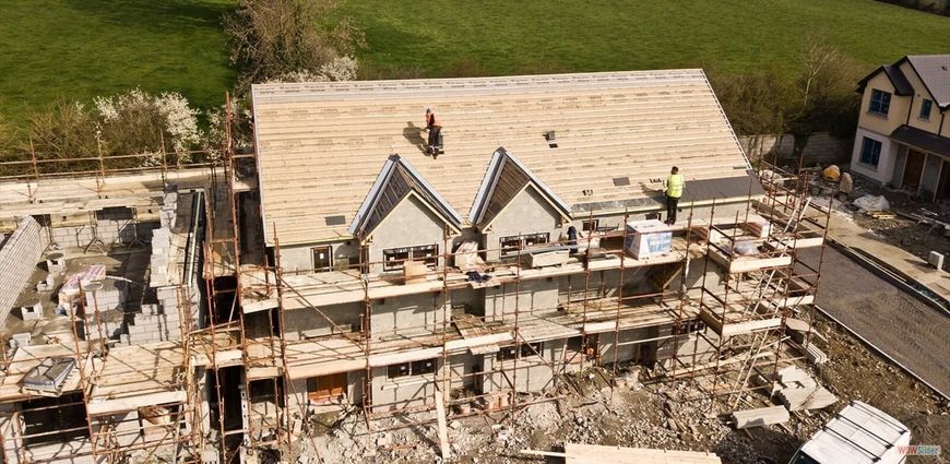 Wood-framed building under construction; plywood walls with window and door openings; tools and materials on the concrete.