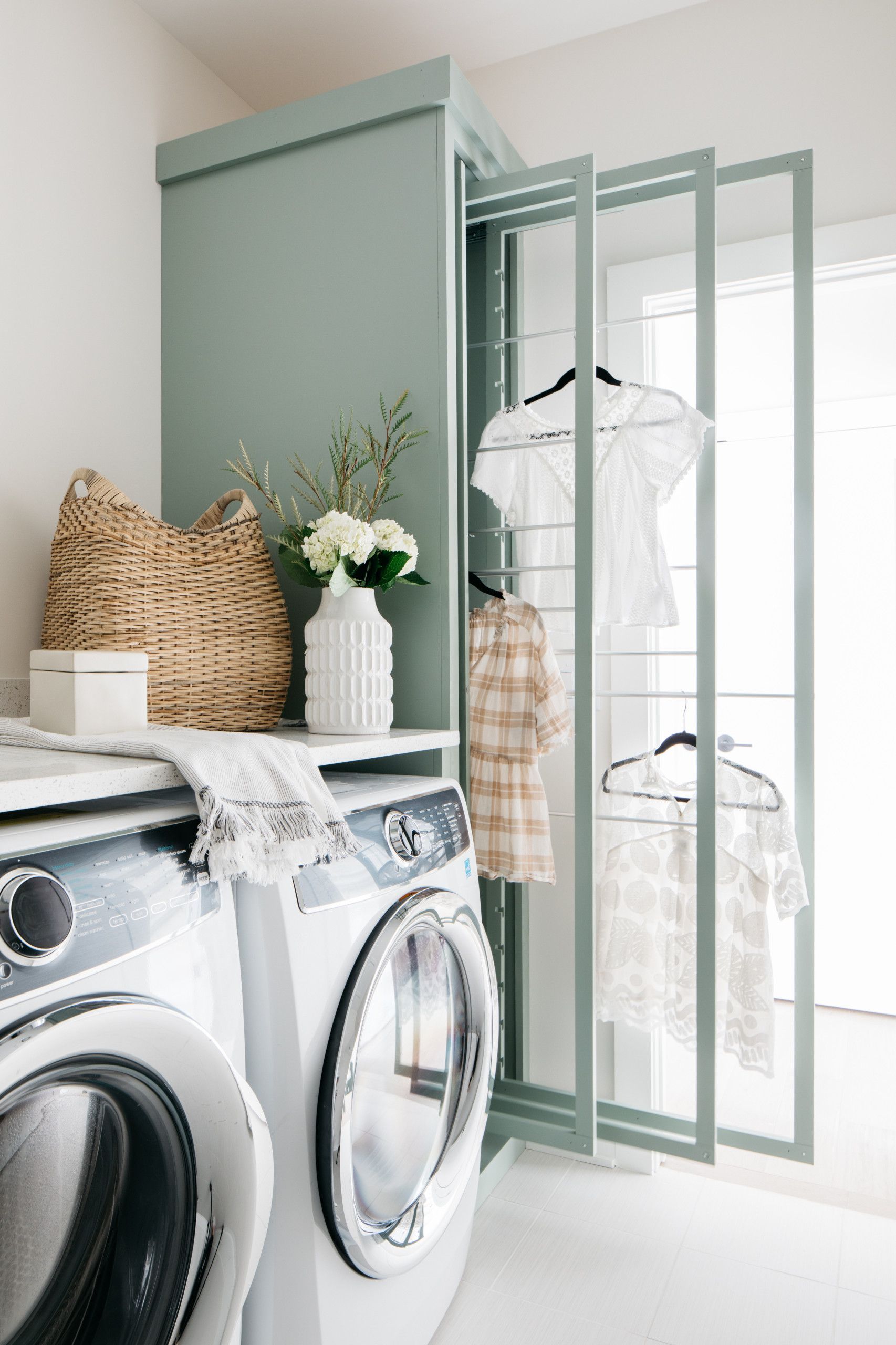 A laundry room with a mint-green cabinet, washing machine, and drying rack holding clothes.