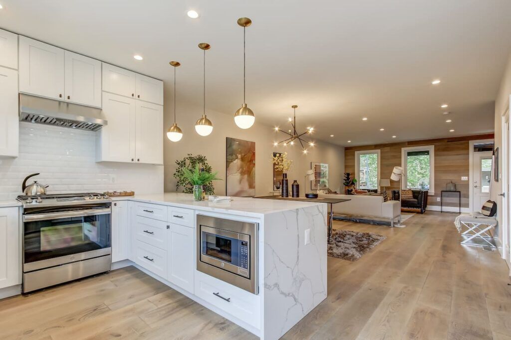 Modern kitchen with white cabinets, marble island, pendant lights, and open concept living space.