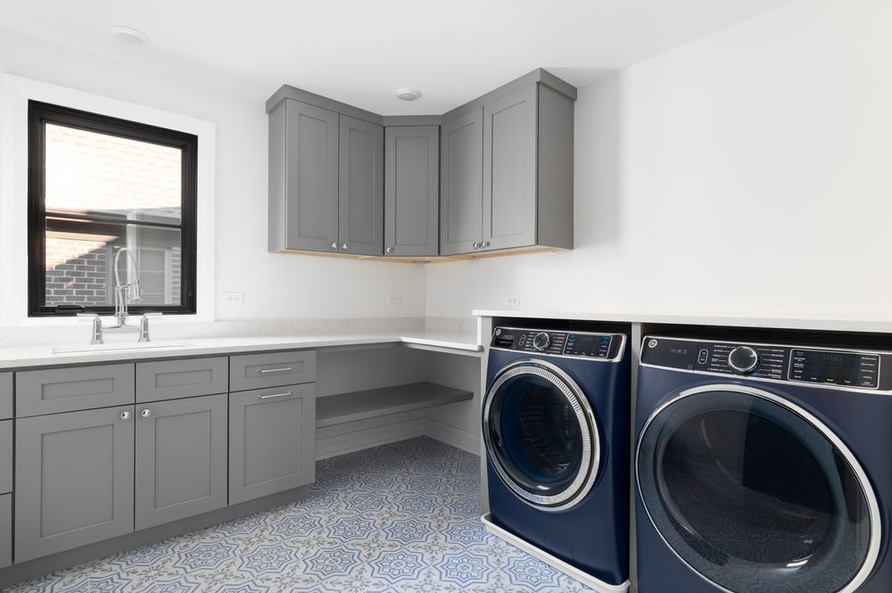 Laundry room with grey cabinets, blue washer and dryer, and window.