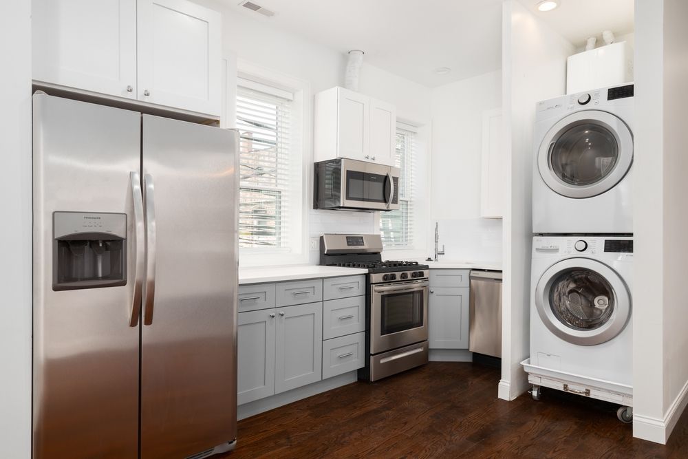 Stainless steel kitchen with fridge, cabinets, oven, and stacked washer/dryer.