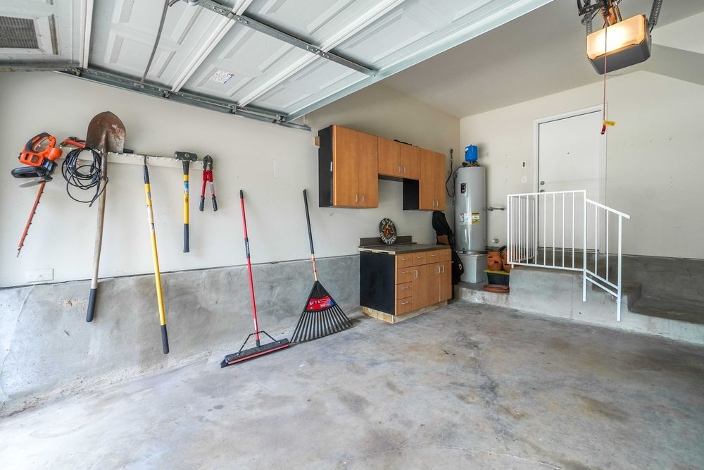 Garage interior with tools hanging on the wall, storage cabinets, and a water heater near a doorway.