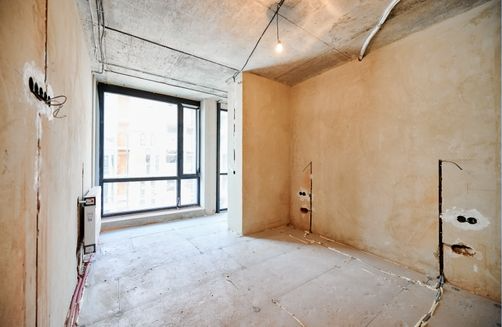 Empty room under construction with a large window and exposed wires.