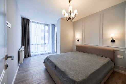 Bedroom with bed, window, chandelier, wall sconces, and neutral color scheme.