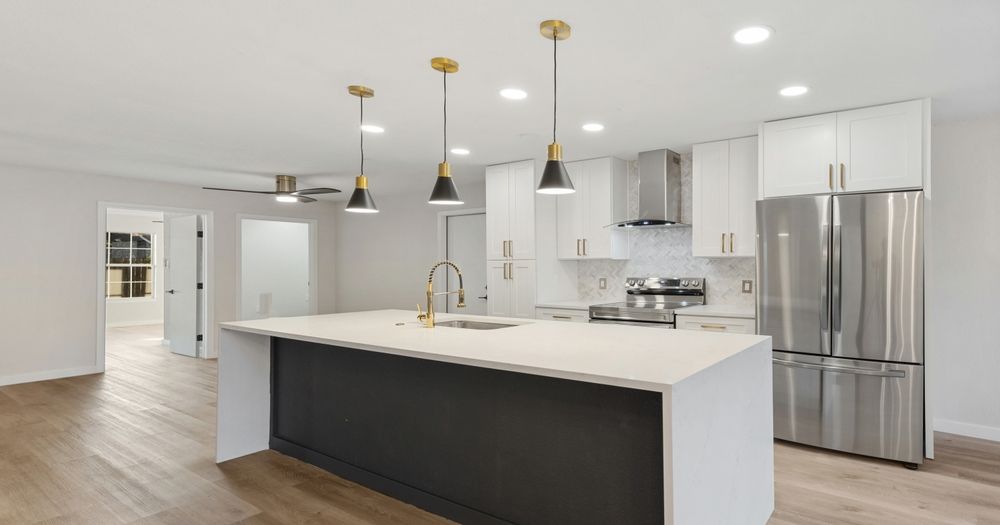 Modern kitchen with white cabinets, dark island, stainless steel appliances, and gold pendant lights.