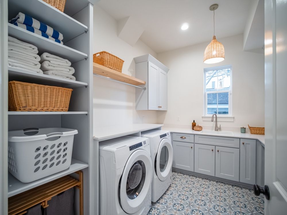 Laundry room with white appliances, gray cabinets, patterned floor, and wicker baskets.