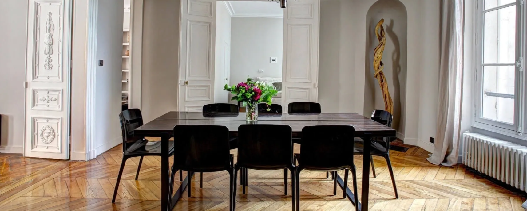 A dining room with a table and chairs and a vase of flowers on the table.