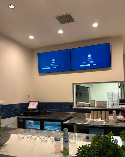 A kitchen with two screens on the wall above the counter.