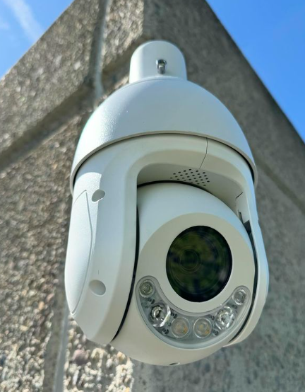 A white security camera is mounted to a concrete wall